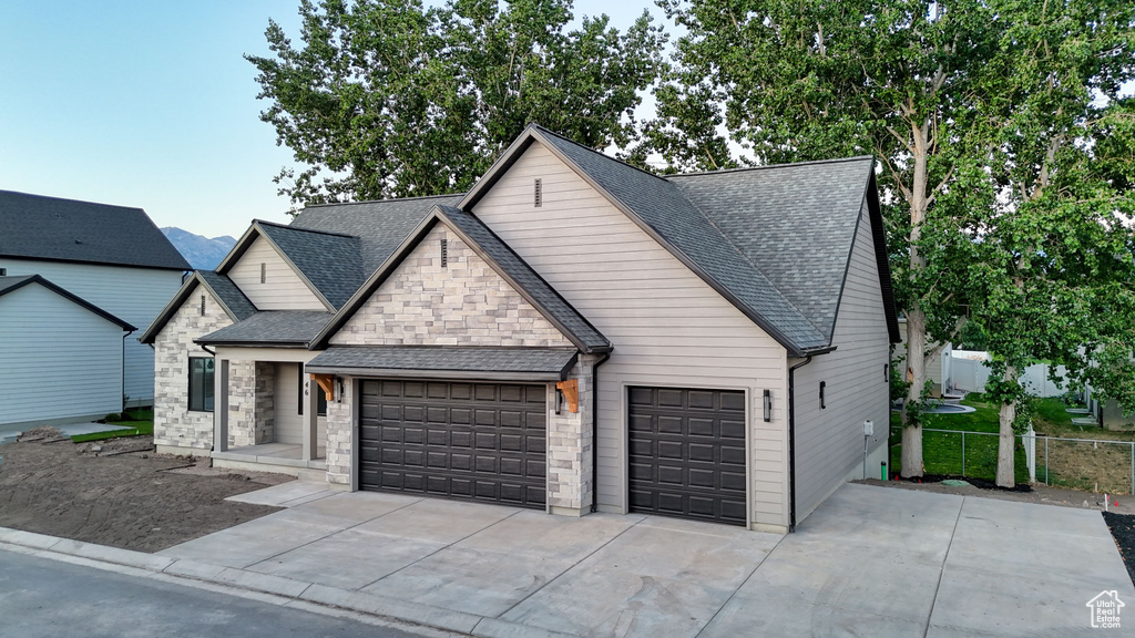View of front of house featuring a garage, concrete driveway, roof with shingles, and stone siding