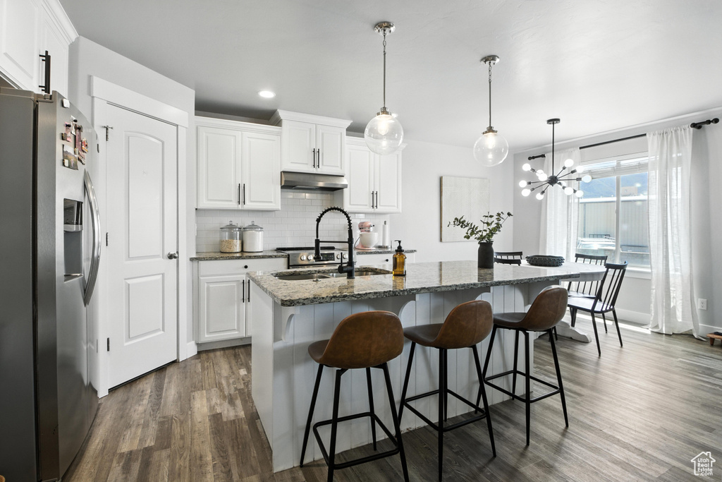 Kitchen with stainless steel refrigerator with ice dispenser, under cabinet range hood, dark wood-type flooring, a breakfast bar, and backsplash