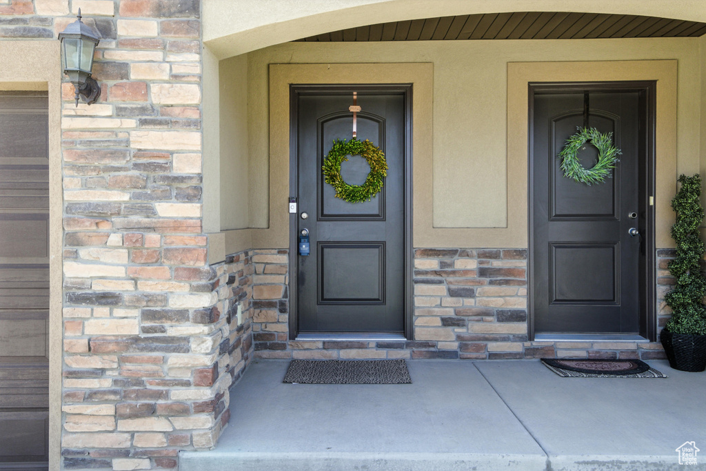 Property entrance featuring stucco siding, stone siding, and covered porch