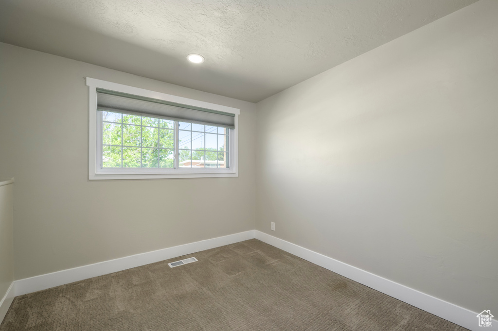 Empty room with dark carpet and a textured ceiling