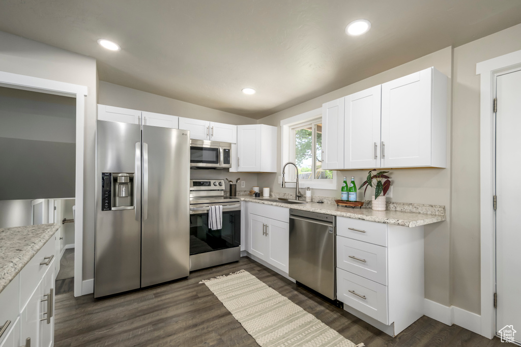 Kitchen with appliances with stainless steel finishes, white cabinets, dark wood-type flooring, and recessed lighting
