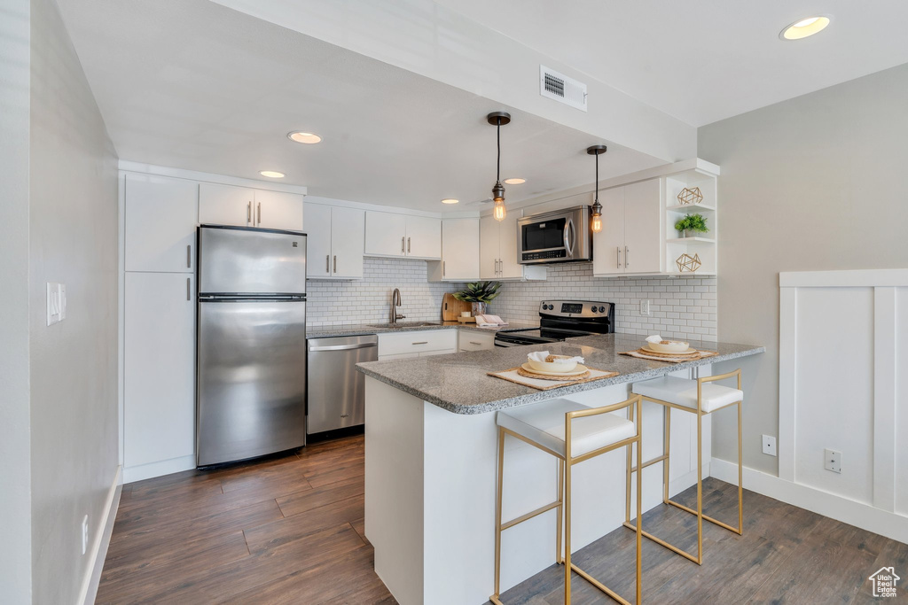 Kitchen featuring appliances with stainless steel finishes, a peninsula, tasteful backsplash, dark wood-style floors, and recessed lighting