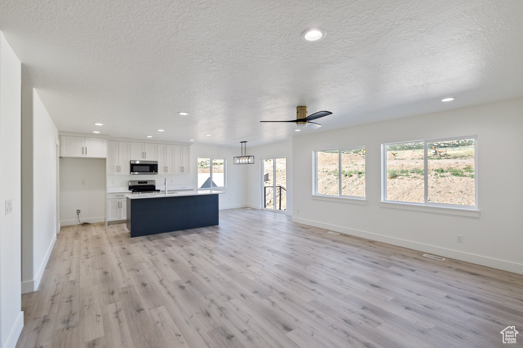 Unfurnished living room featuring light wood-type flooring, a ceiling fan, recessed lighting, and a textured ceiling