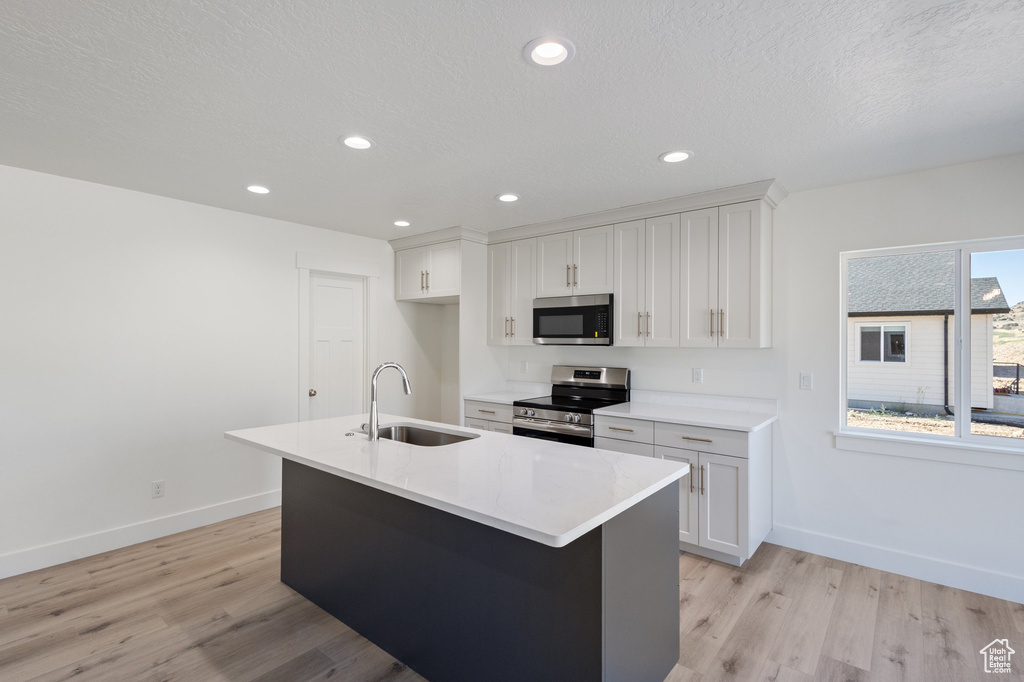 Kitchen with appliances with stainless steel finishes, light wood-type flooring, white cabinets, recessed lighting, and a textured ceiling
