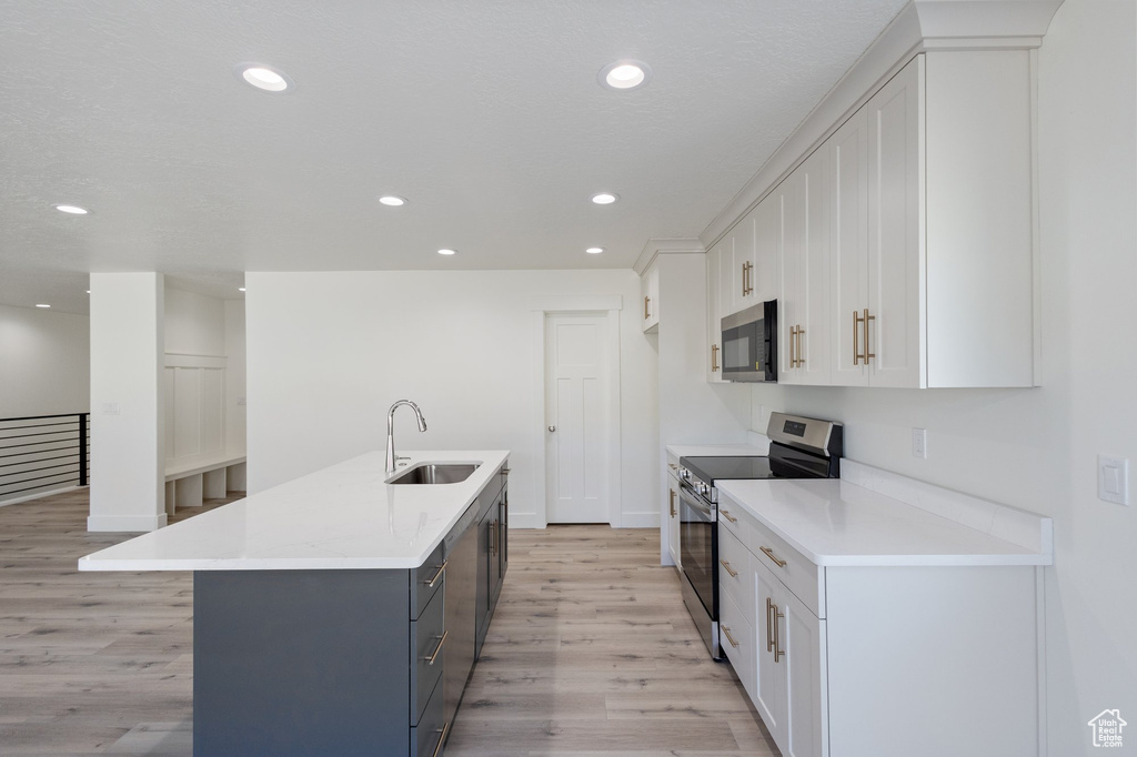 Kitchen featuring appliances with stainless steel finishes, light wood-type flooring, white cabinets, a center island with sink, and light countertops