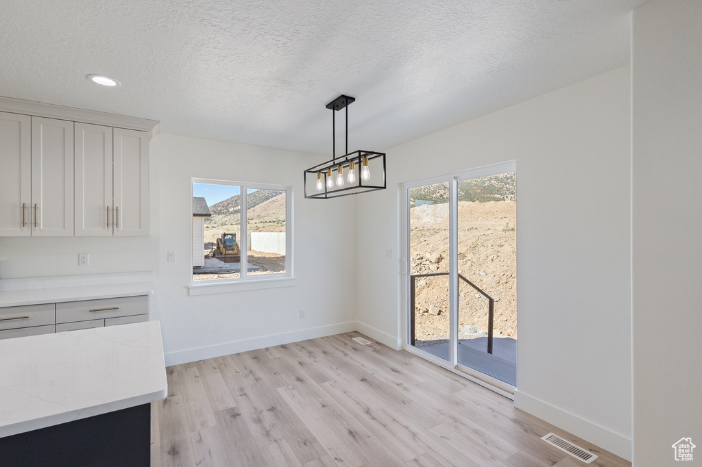 Unfurnished dining area featuring light wood finished floors, a textured ceiling, recessed lighting, and a chandelier