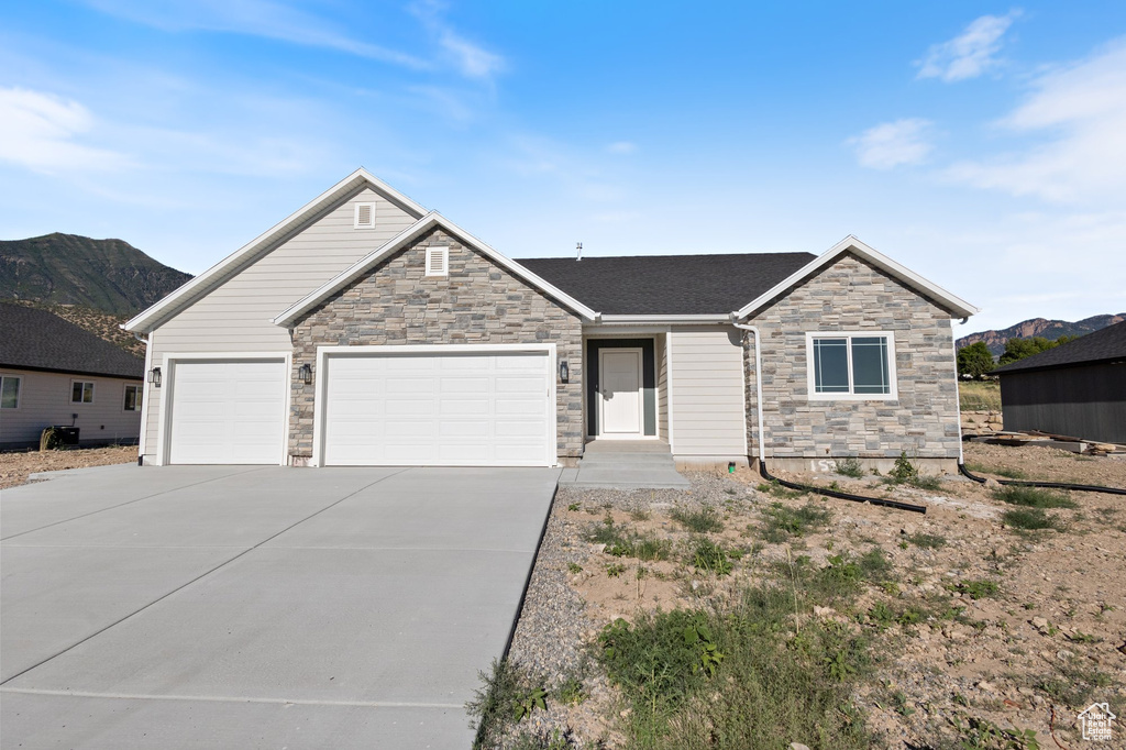 View of front facade with stone siding, driveway, a garage, and a mountain view