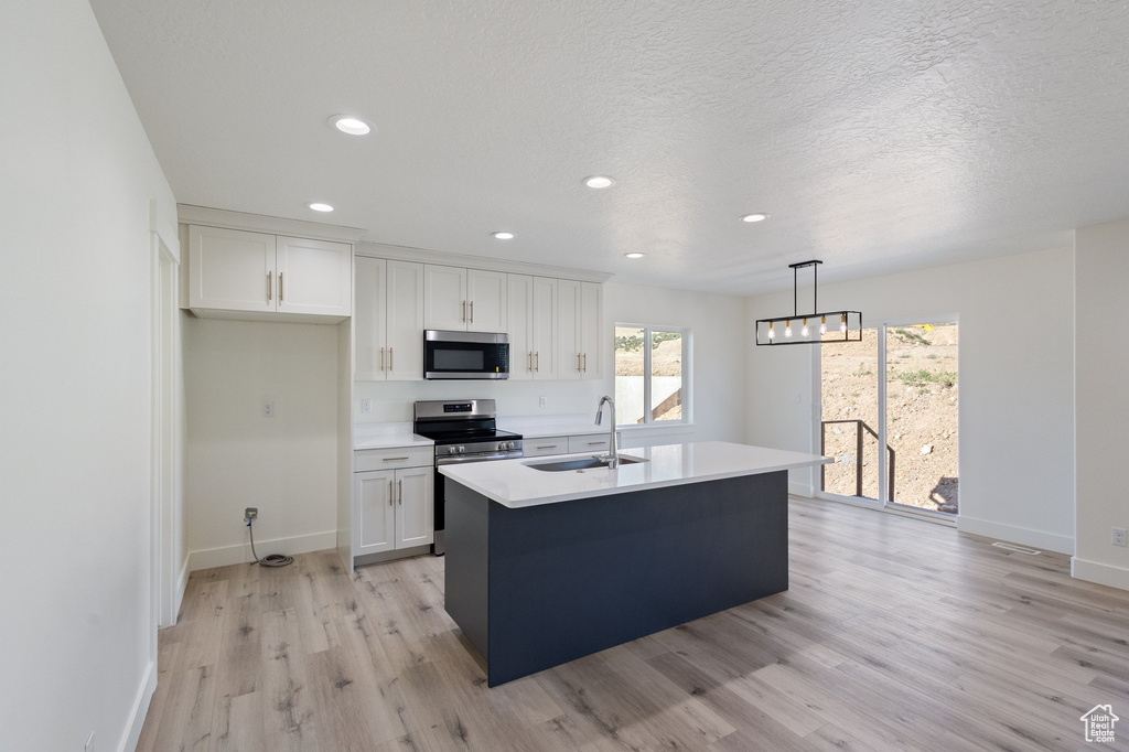 Kitchen with stainless steel appliances, white cabinetry, light wood-style flooring, recessed lighting, and a textured ceiling