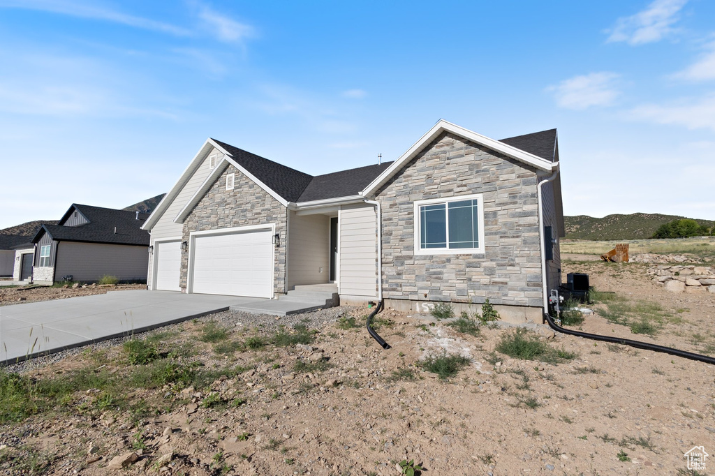 View of front facade featuring stone siding, driveway, and a garage