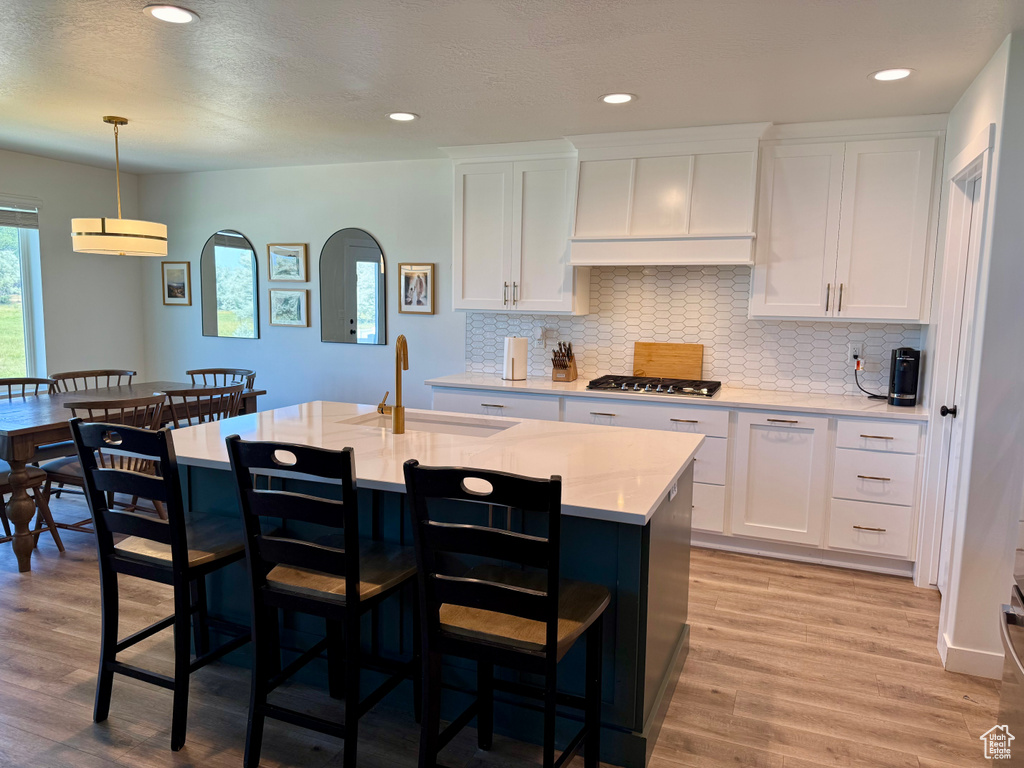 Kitchen featuring white cabinets, decorative backsplash, a kitchen breakfast bar, stainless steel gas cooktop, and recessed lighting