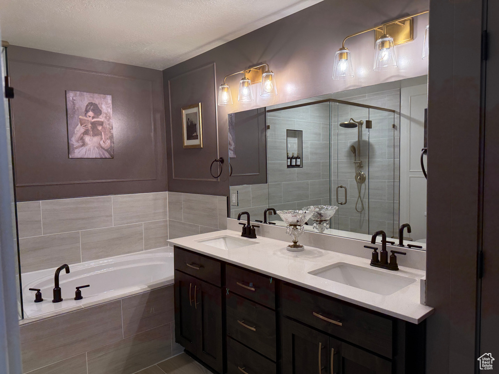 Full bathroom featuring double vanity, a bath, a stall shower, and a textured ceiling