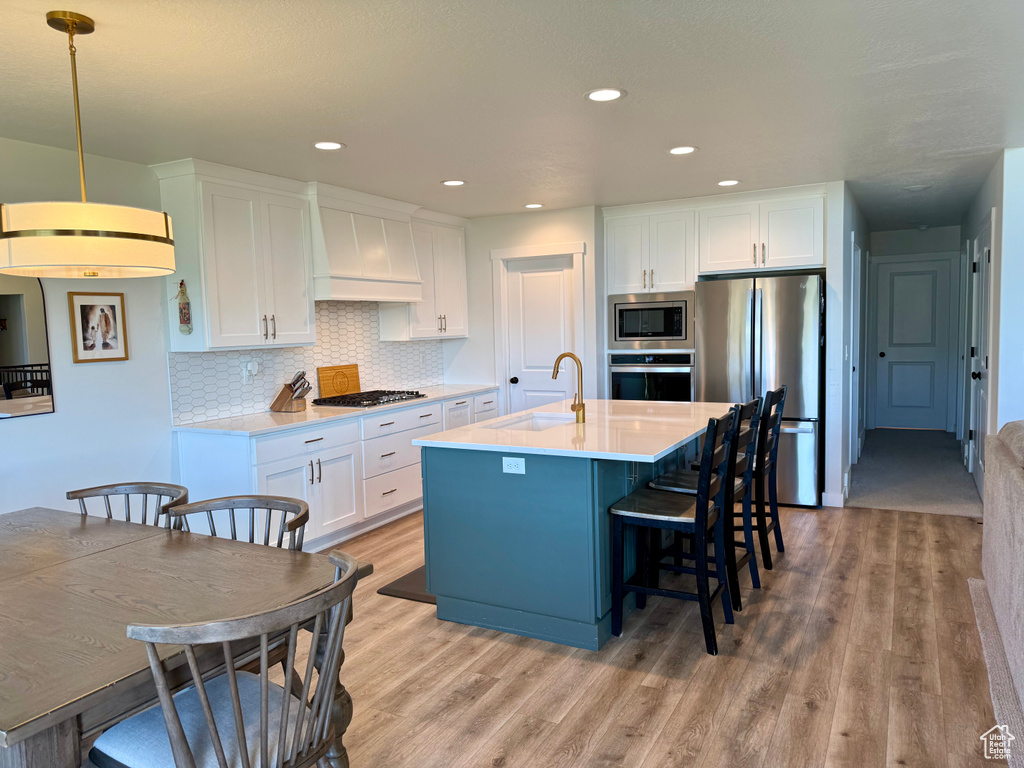 Kitchen featuring stainless steel appliances, premium range hood, light wood finished floors, white cabinetry, and recessed lighting
