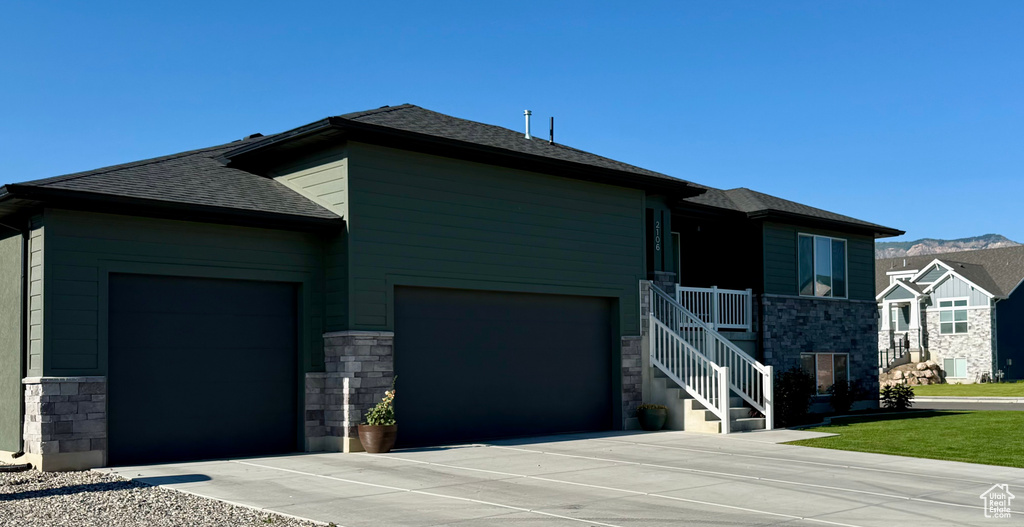 View of front of house with stone siding, a garage, a shingled roof, and concrete driveway