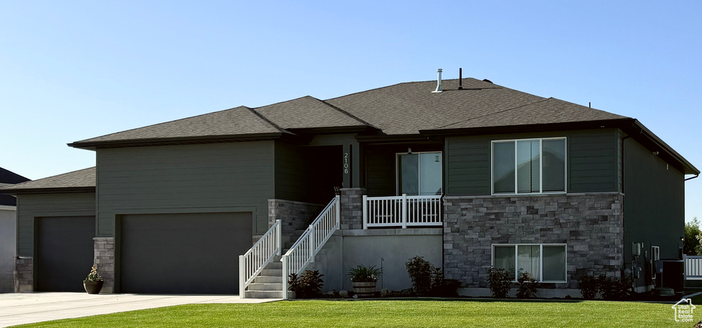 Prairie-style house with stone siding, concrete driveway, a front lawn, an attached garage, and a porch