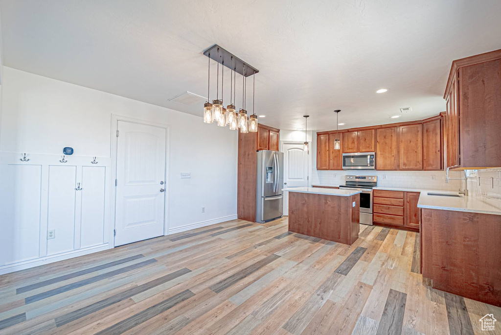 Kitchen featuring stainless steel appliances, a center island, light wood-style flooring, brown cabinetry, and decorative backsplash
