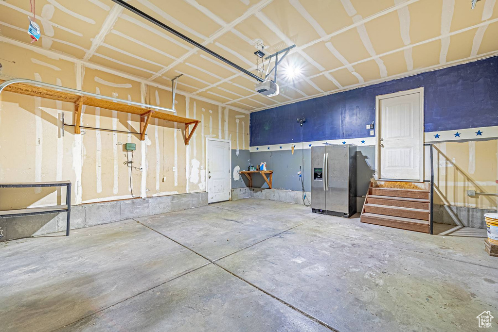 Garage featuring stainless steel fridge with ice dispenser and a garage door opener
