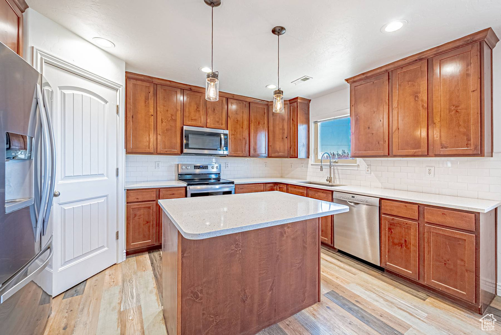 Kitchen with appliances with stainless steel finishes, light wood-type flooring, brown cabinets, and recessed lighting