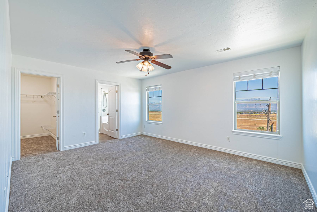 Unfurnished bedroom featuring carpet, a spacious closet, ceiling fan, and ensuite bathroom