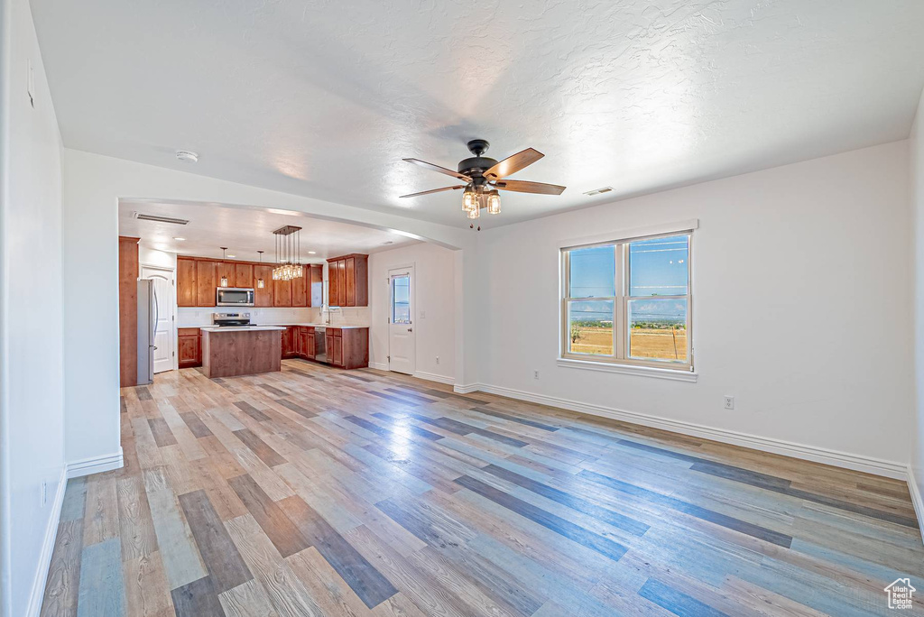 Unfurnished living room with ceiling fan, light wood finished floors, and arched walkways