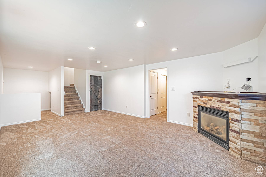Unfurnished living room with a stone fireplace, stairs, recessed lighting, and carpet