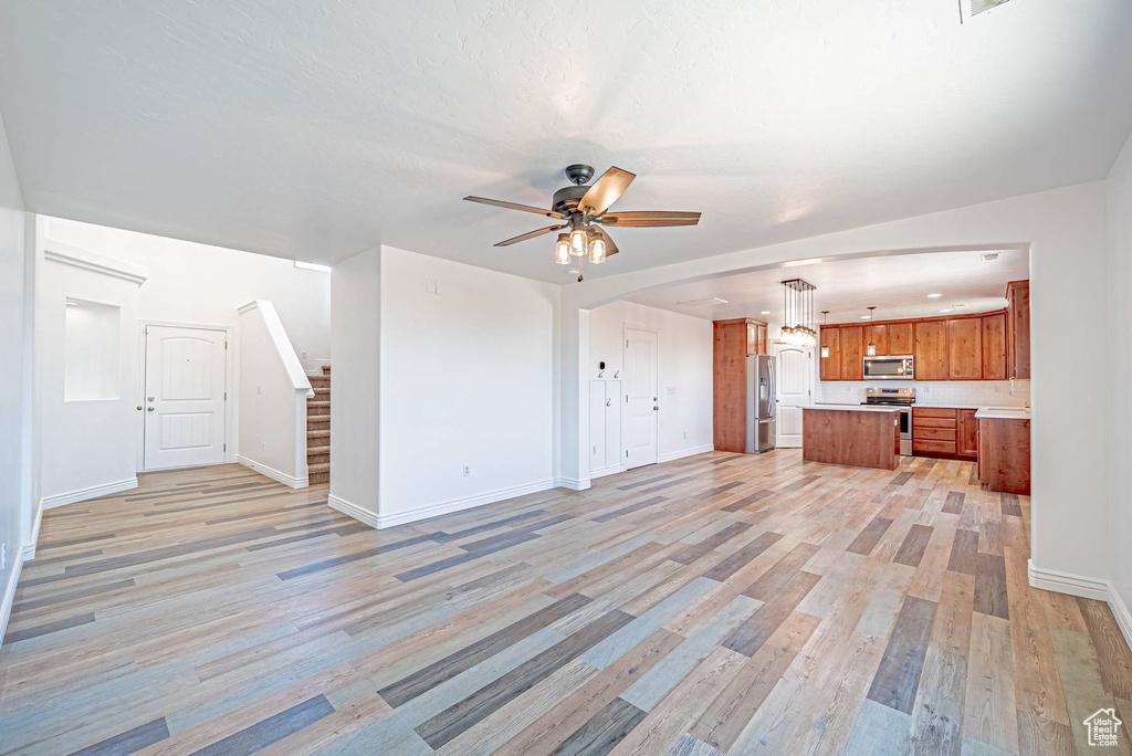 Unfurnished living room featuring light wood-style flooring, a ceiling fan, and stairway