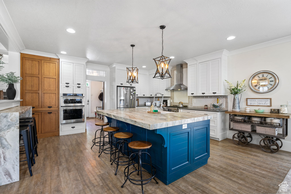 Kitchen featuring wall chimney range hood, appliances with stainless steel finishes, white cabinets, backsplash, and recessed lighting