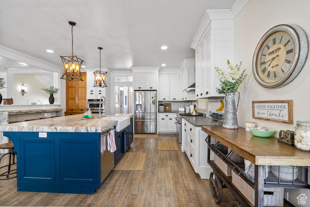 Kitchen with stainless steel appliances, blue cabinetry, white cabinetry, decorative backsplash, and dark wood-style floors