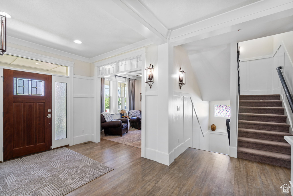 Entrance foyer with a decorative wall, wood finished floors, stairs, and crown molding