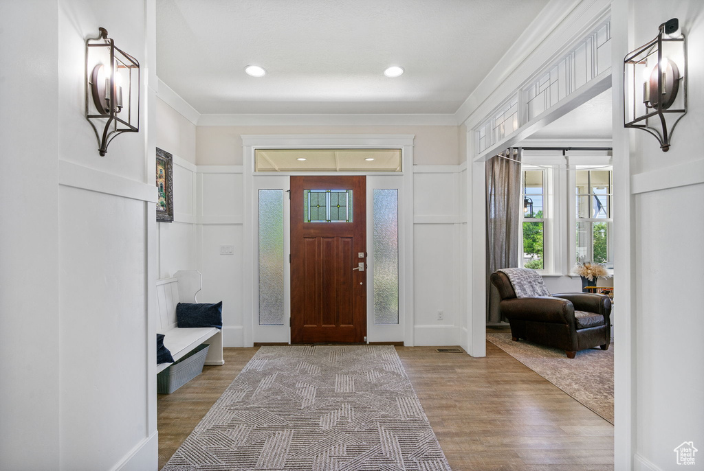Entryway featuring wood finished floors, a decorative wall, ornamental molding, and recessed lighting