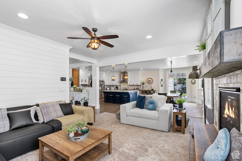 Living room featuring a ceiling fan, a brick fireplace, recessed lighting, ornamental molding, and light wood-style flooring