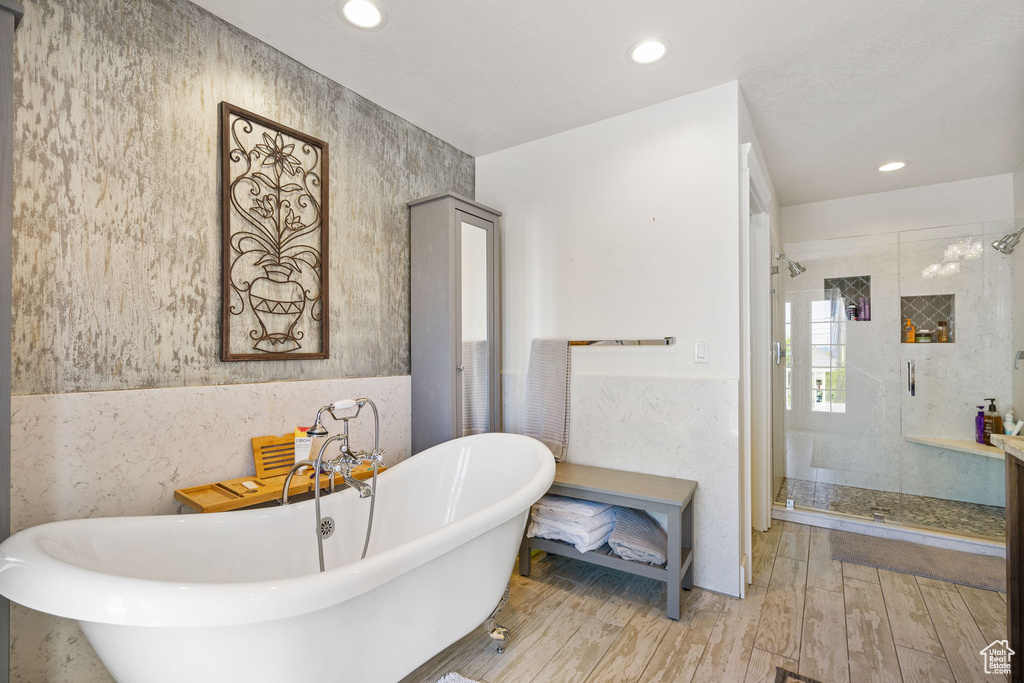 Bathroom with a stall shower, a soaking tub, recessed lighting, wood finished floors, and tile walls