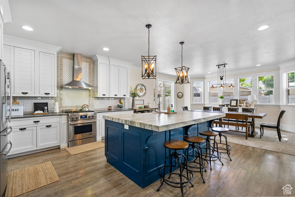 Kitchen with stainless steel appliances, wall chimney range hood, healthy amount of natural light, white cabinets, and recessed lighting