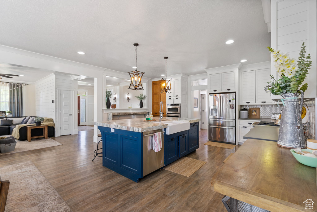 Kitchen featuring blue cabinetry, appliances with stainless steel finishes, open floor plan, dark wood-style flooring, and recessed lighting