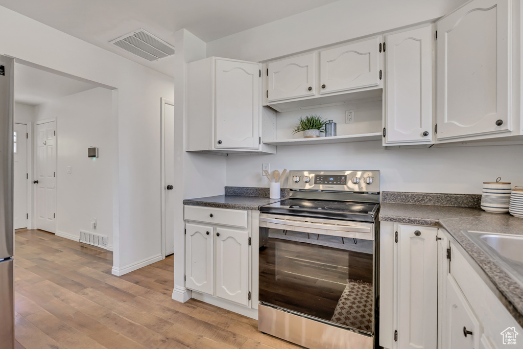 Kitchen with stainless steel range with electric cooktop, white cabinetry, dark countertops, light wood-type flooring, and open shelves