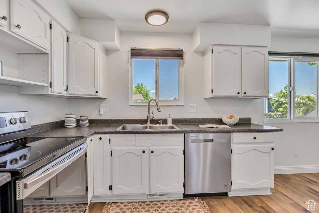 Kitchen featuring appliances with stainless steel finishes, dark countertops, white cabinets, and light wood-style flooring