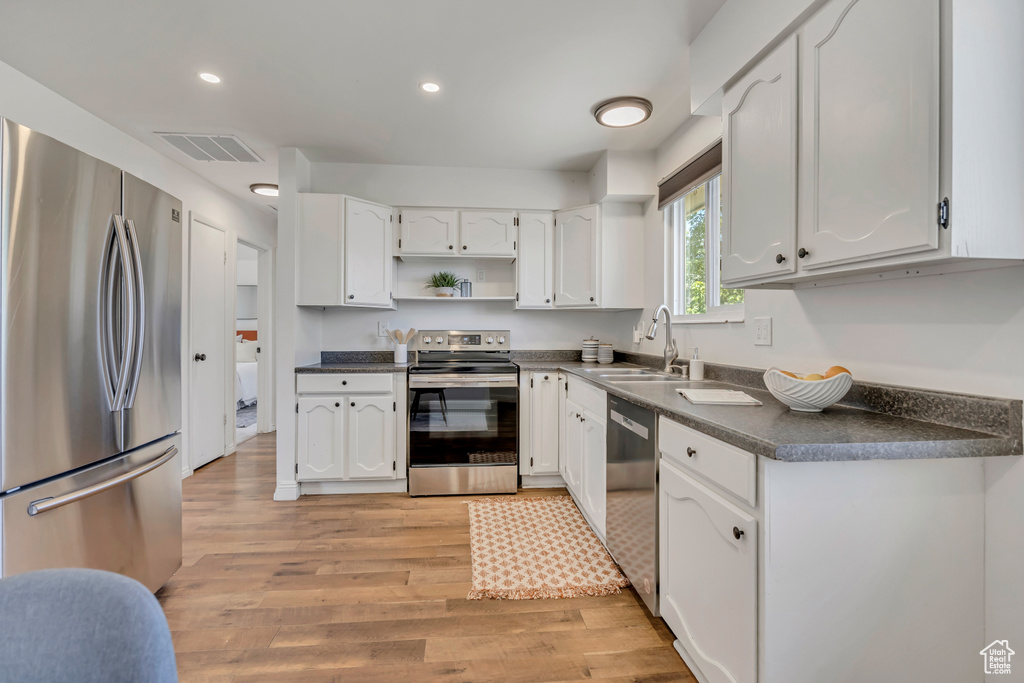 Kitchen with stainless steel appliances, dark countertops, open shelves, white cabinets, and recessed lighting
