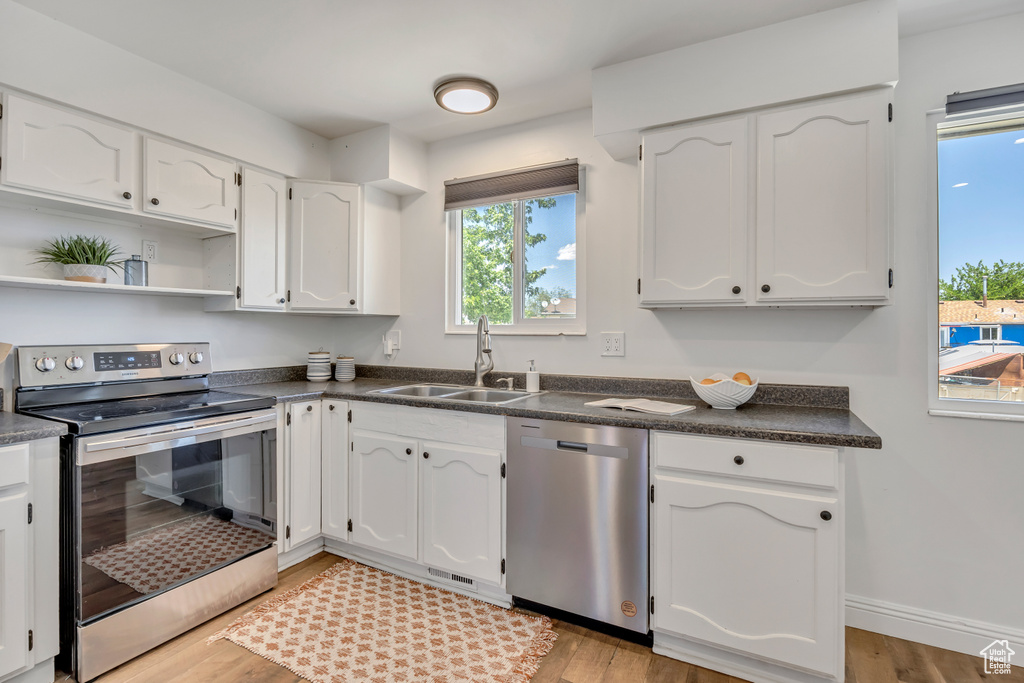 Kitchen featuring stainless steel appliances, dark countertops, white cabinetry, and light wood-style floors