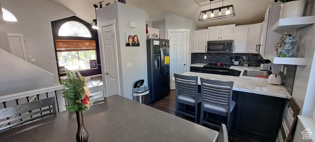 Kitchen featuring black appliances, backsplash, white cabinetry, dark wood-type flooring, and a peninsula
