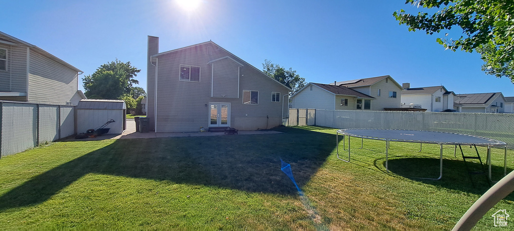 Rear view of property with a trampoline, a fenced backyard, french doors, a chimney, and a residential view