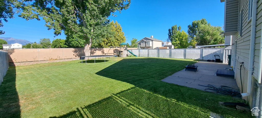 Fenced backyard with a playground, a patio area, and a trampoline