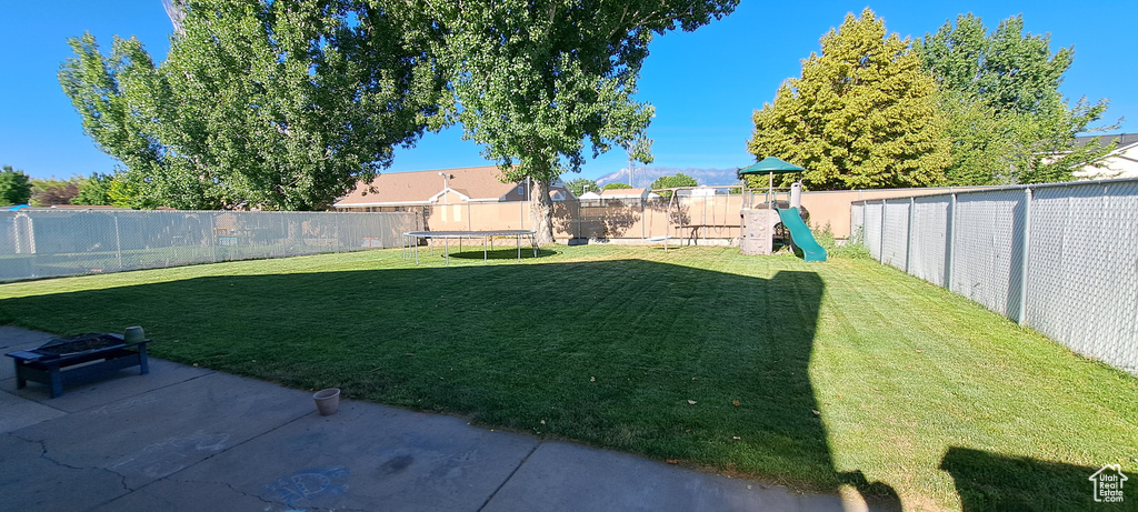 Fenced backyard featuring a trampoline, a playground, and a patio