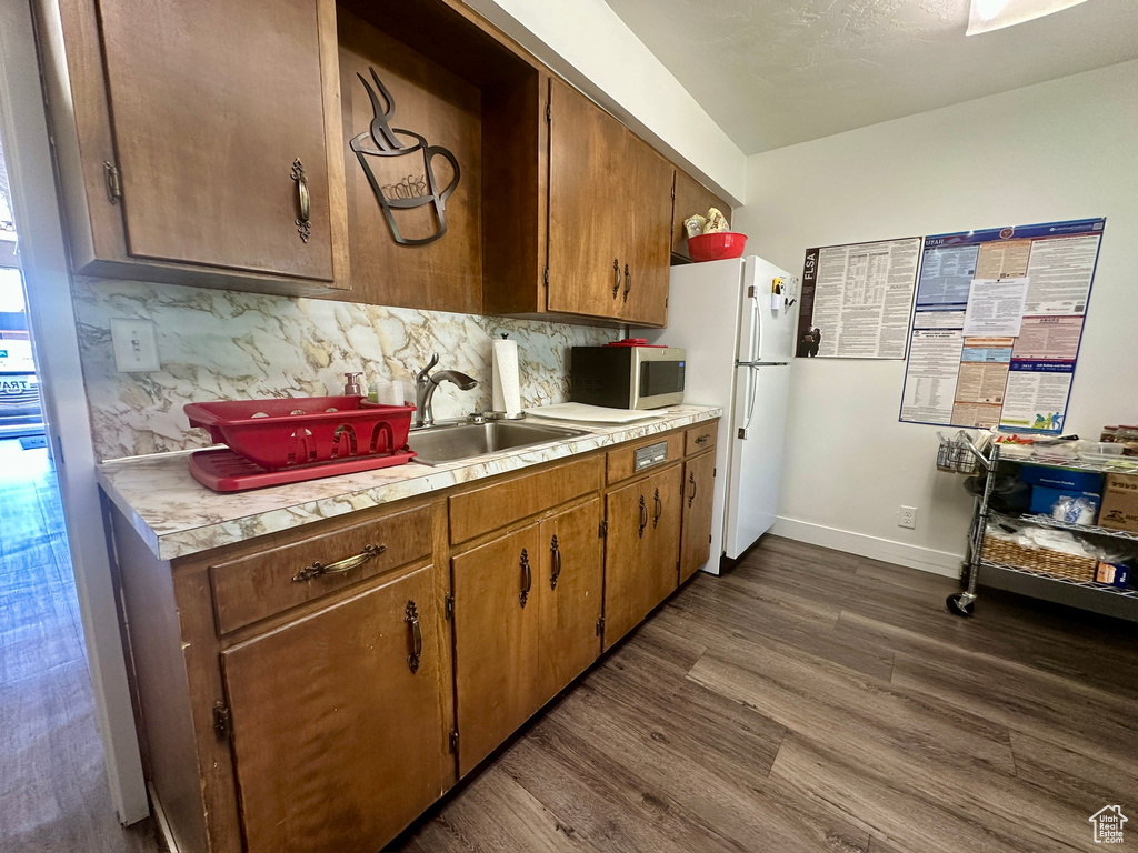 Kitchen featuring freestanding refrigerator, light countertops, decorative backsplash, and dark wood-style flooring