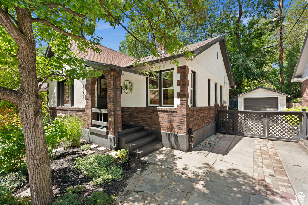 View of front facade featuring brick siding, a garage, an outdoor structure, and roof with shingles
