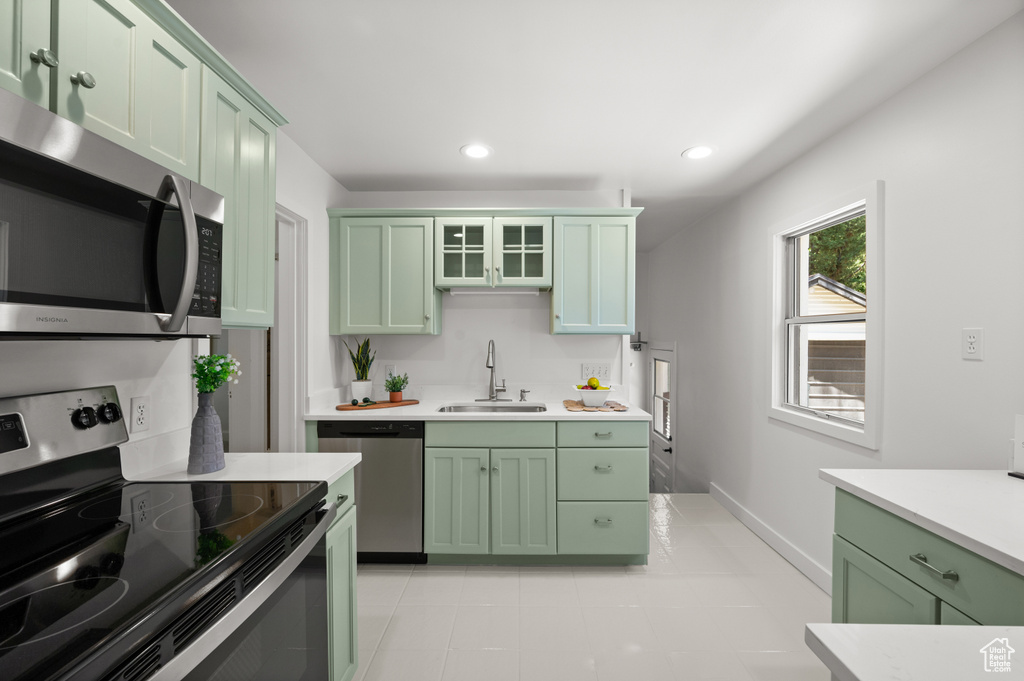 Kitchen featuring green cabinets, appliances with stainless steel finishes, light countertops, recessed lighting, and glass insert cabinets