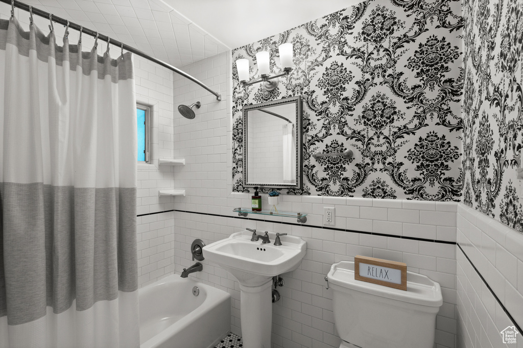 Bathroom with wallpapered walls, shower / bath combo, wainscoting, and tile walls