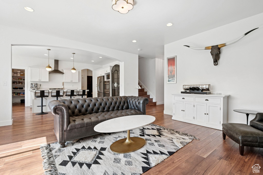 Living area featuring arched walkways, stairs, wood finished floors, and recessed lighting