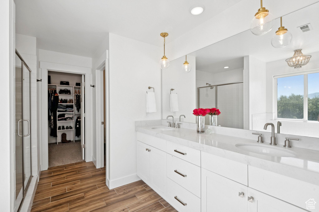 Bathroom featuring a stall shower, wood finished floors, a spacious closet, double vanity, and recessed lighting