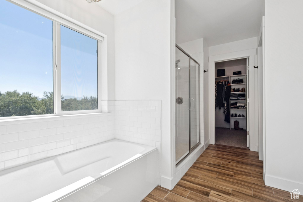 Full bath featuring a shower stall, a garden tub, a spacious closet, and wood finished floors