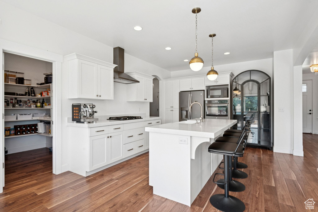 Kitchen featuring black appliances, wall chimney exhaust hood, arched walkways, light countertops, and recessed lighting