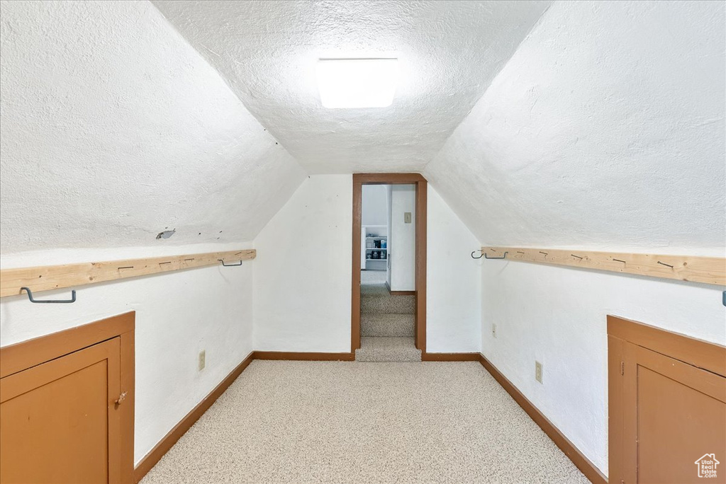 Additional living space featuring a textured ceiling, light carpet, and lofted ceiling